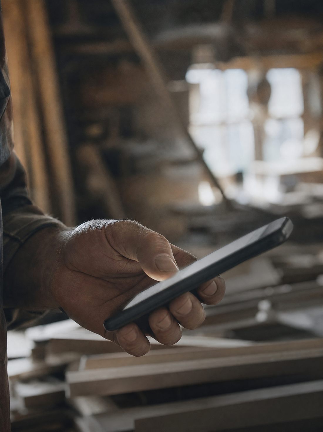 Handwerker schaut in seiner Werkstatt auf ein Smartphone
